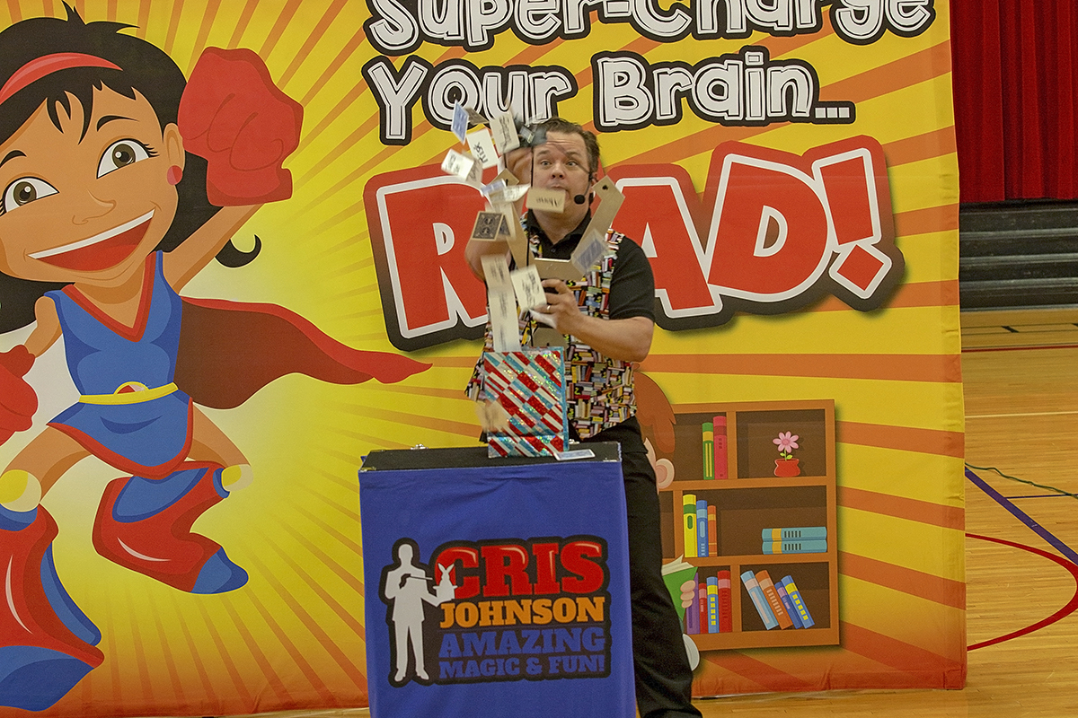 school assembly presenter Cris Johnson at a read across america school assembly throwing cards